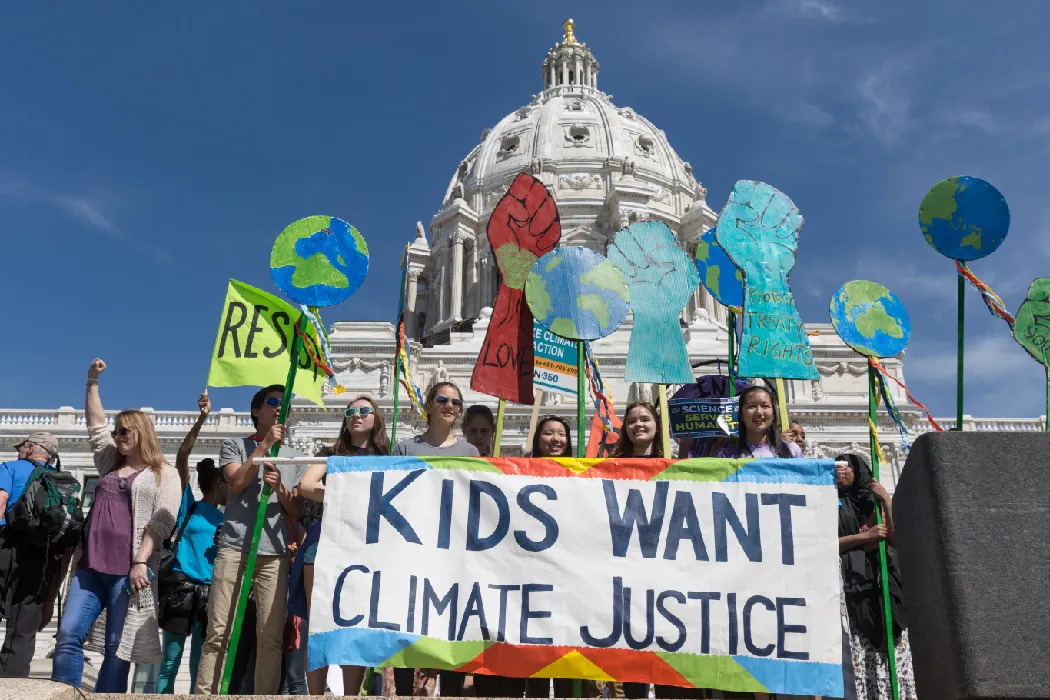 Young people rally in front of a government building holding a sign that says Kids Want Climate Justice.