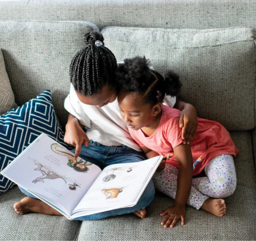 Photo of two young children sitting on a couch looking at a book together.