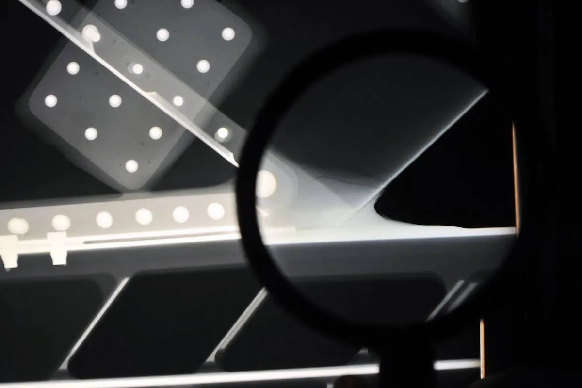 On a screen is an X-ray image of components connected at angles, with circles showing attachment points. A magnifying glass is visible in front of part of the screen.