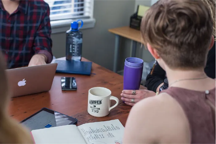 Photo showing three individuals sitting at a table with paperwork and laptops.