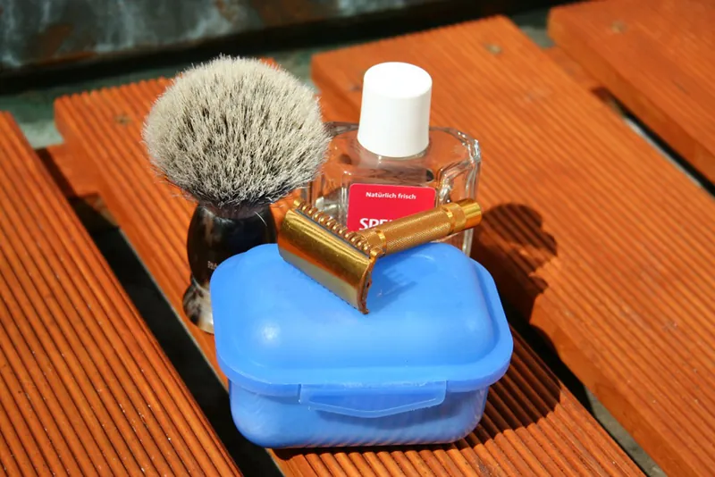 A razor, shave brush, antiseptic, and storage case are grouped together on a table.