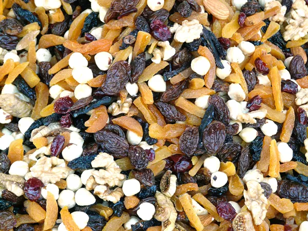 A close-up of a colorful trail mix containing dried apricots, raisins, white chocolate chips, walnuts, hazelnuts, dried cranberries, and other mixed nuts and dried fruits.