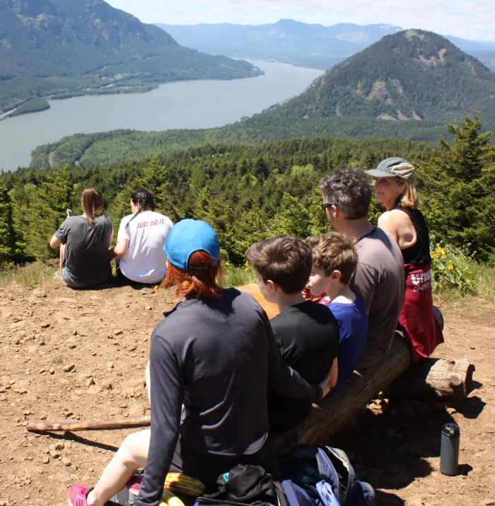 Photo of family with two adults and three adolescents sitting on a bench on a mountain.