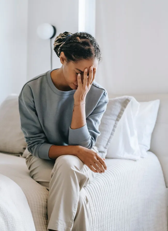Image of woman sitting on a bed with her head in her hand.