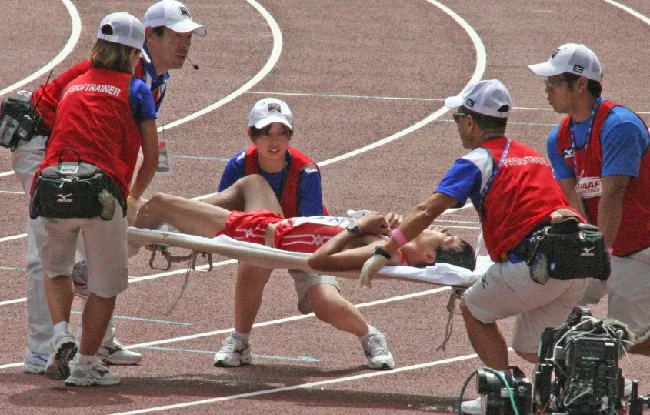 A photo shows an injured runner being carried off the track on a stretcher.