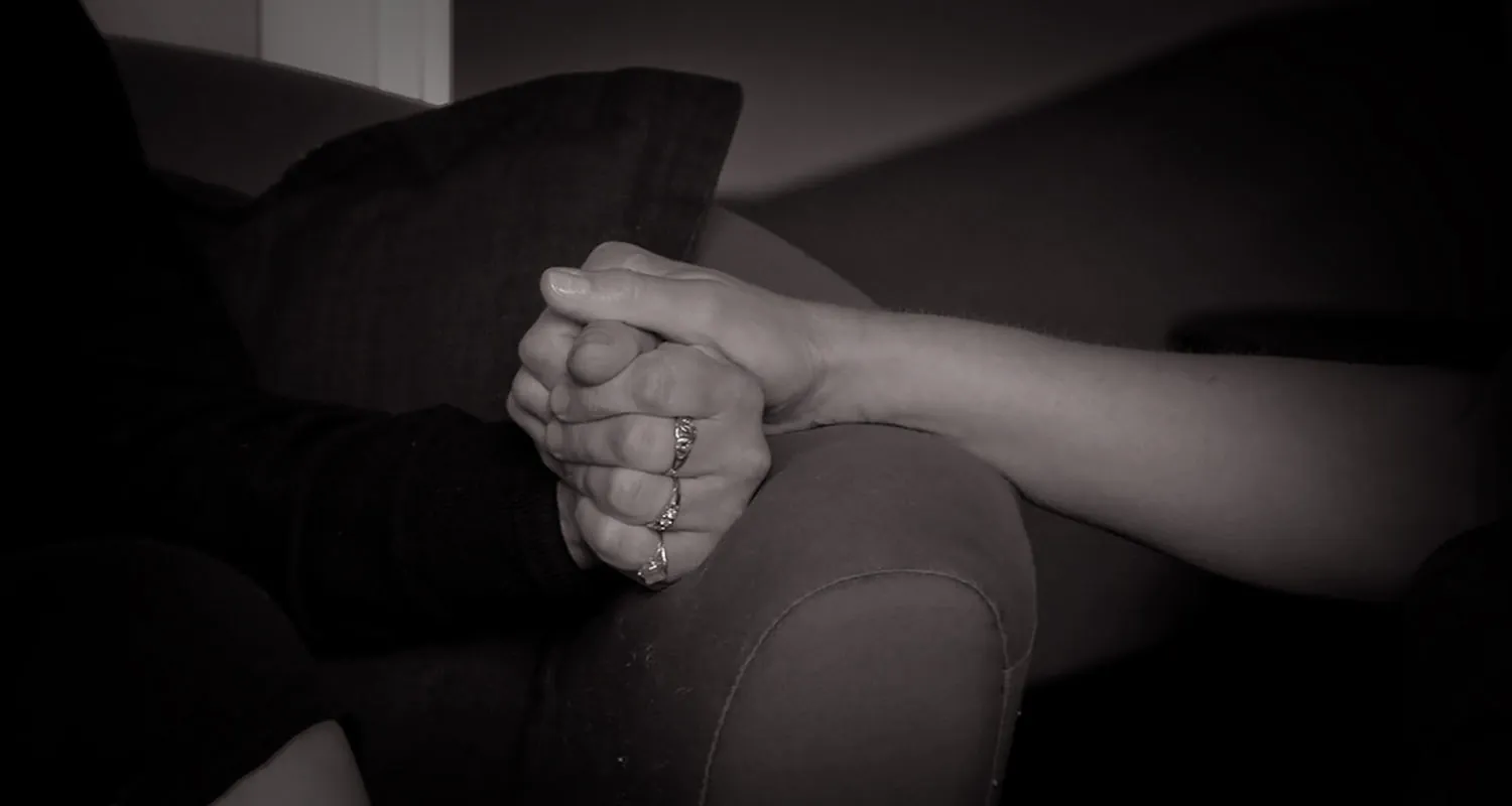 A black and white photograph shows a male hand holding a female hand.