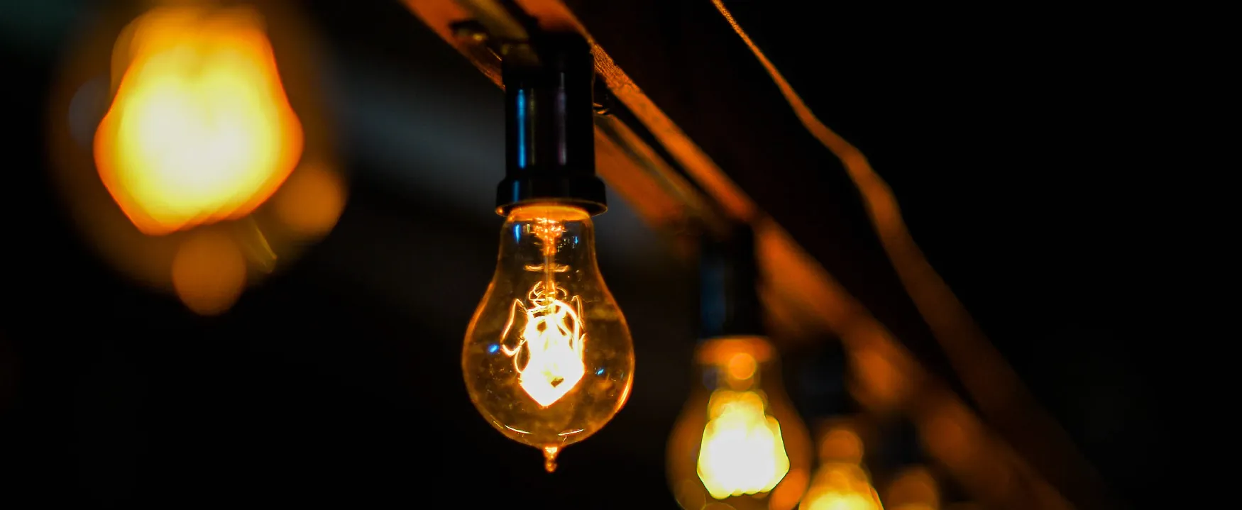 Close-up of a lit Edison bulb, part of a string of warm lights, providing a soft, ambient glow in the dark.