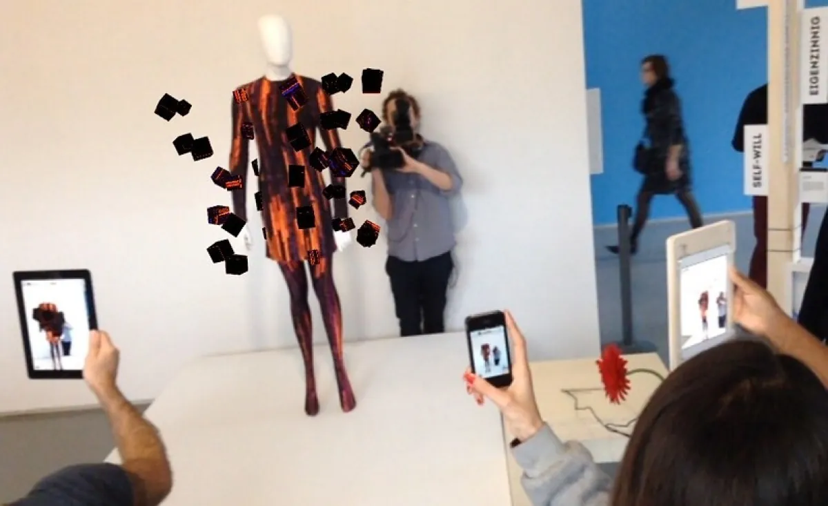 Photo of individuals taking pictures of a dressed mannequin using augmented reality on their devices to picture how a dress would look on different bodies.