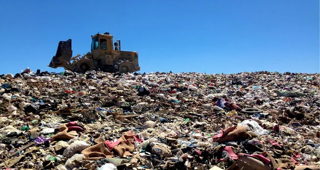 A photo of a bulldozer on top of a large pile of trash.
