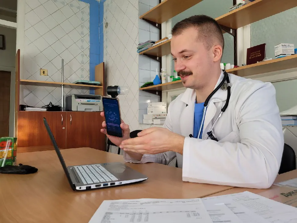 Photo of healthcare worker using a laptop and their cellphone in a medical setting.