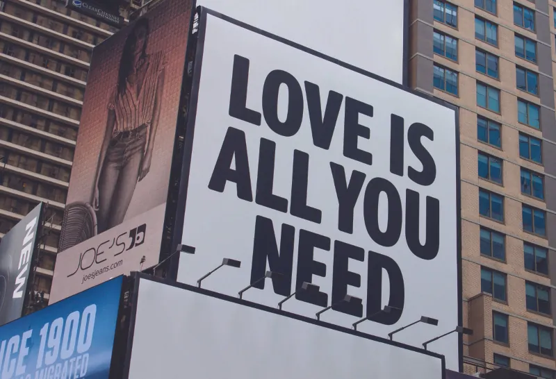 This image shows a billboard on the side of a building that says love is all you need.