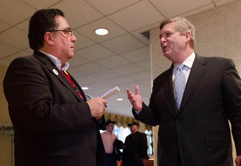 Two men speak to each other in a hallway.