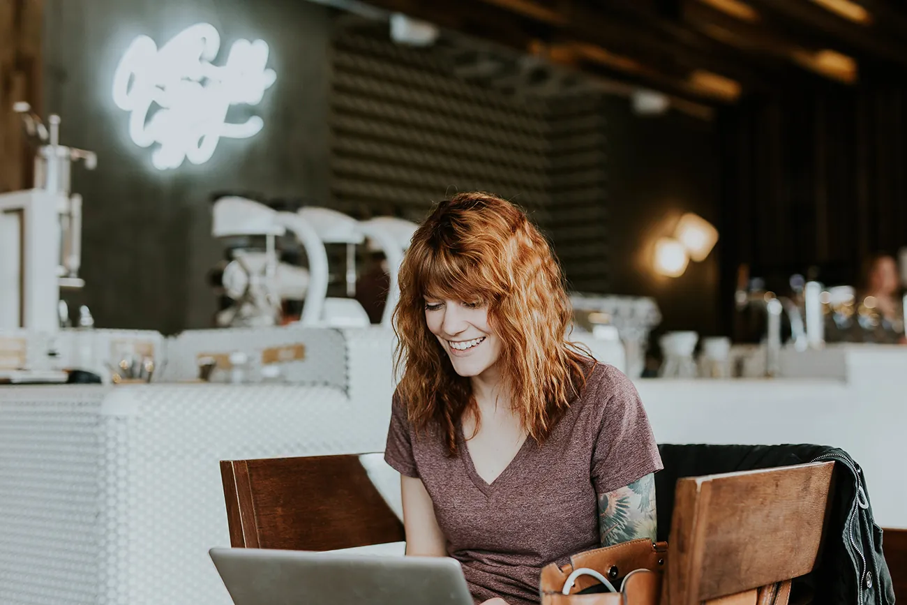 A photograph shows a woman on a laptop while she sits at a coffee shop.