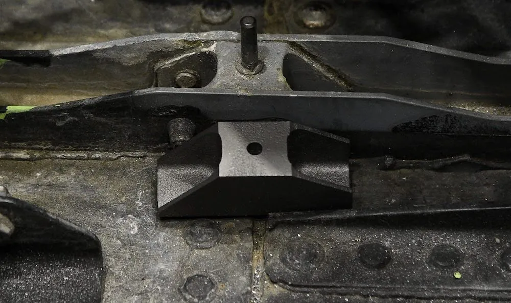 Two brackets identical in shape are next to each other. The installed part is bolted onto the surface and shows signs of wear.