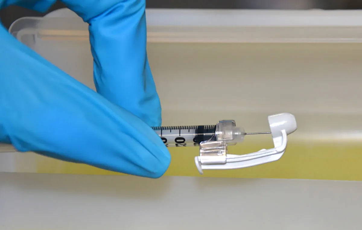 A photograph of a syringe held between thumb and forefinger.