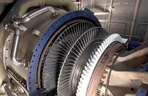Close-up of a large industrial turbine's open casing, revealing multiple stages of compressor blades during maintenance or assembly. The intricate design highlights the complex engineering of power generation.