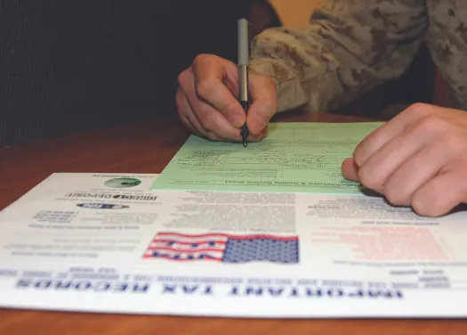 An image of a person’s hand, holding a pen over a form.