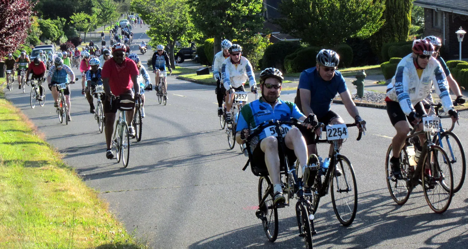 Photo of many people riding bicycles, some upright and some recumbent. All are wearing helmets.