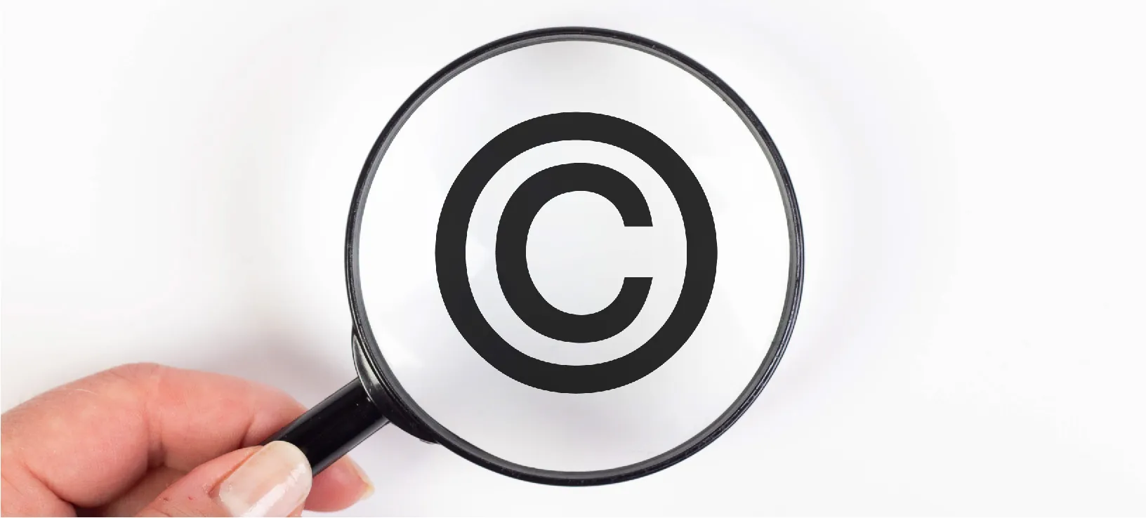 A hand holding a magnifying glass enlarging a copyright symbol.