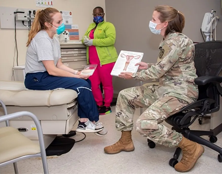 Photo of military medical personnel showing an image of a uterus to a patient on a bed while a nurse looks on from the back.