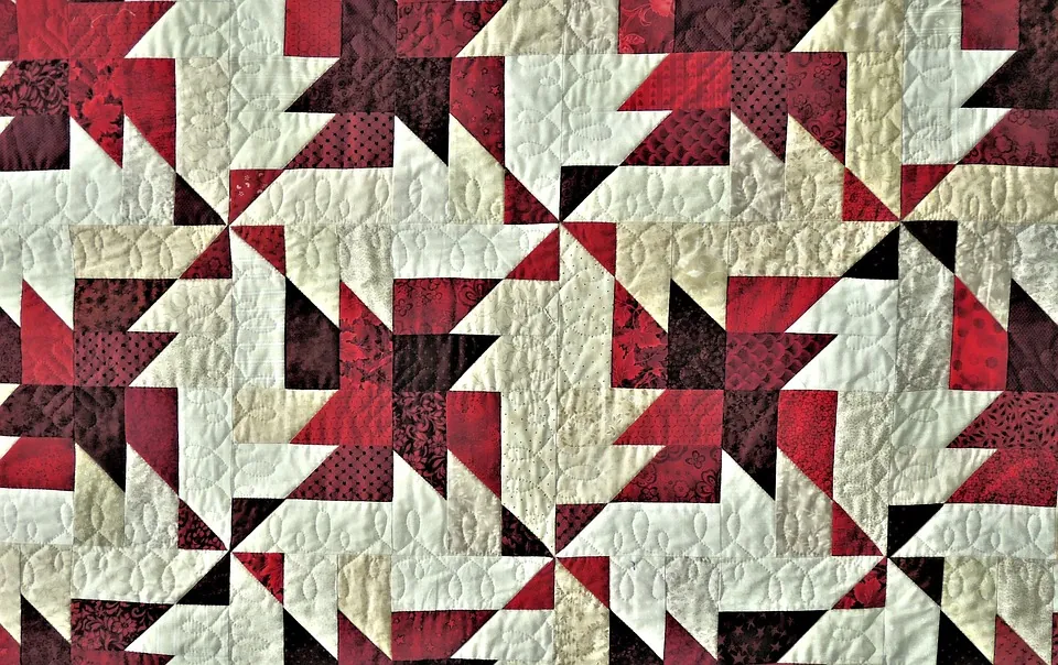 Intricate quilt pattern featuring a striking array of red, maroon, and cream geometric shapes, creating a dynamic and visually rich textile with delicate quilting stitches.