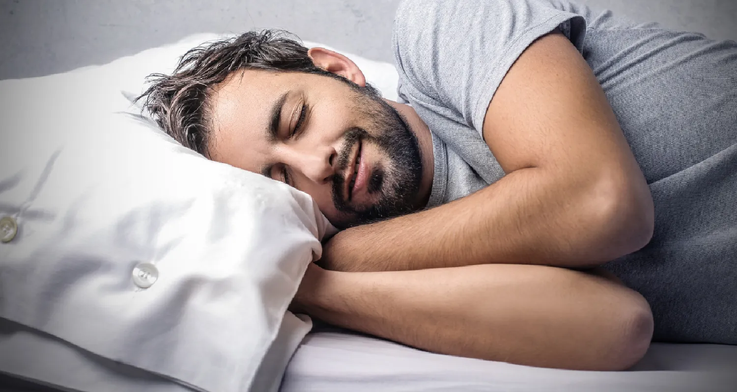 Photo of man sleeping in a bed with a smile on his face.