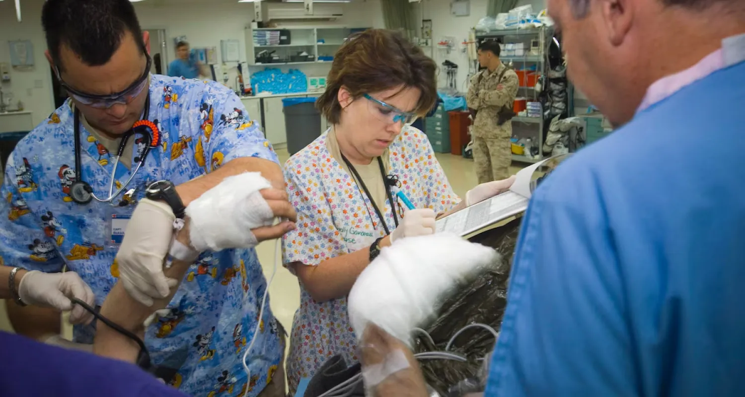A color photograph shows several nurses overlooking a patient whose hands are bandaged.