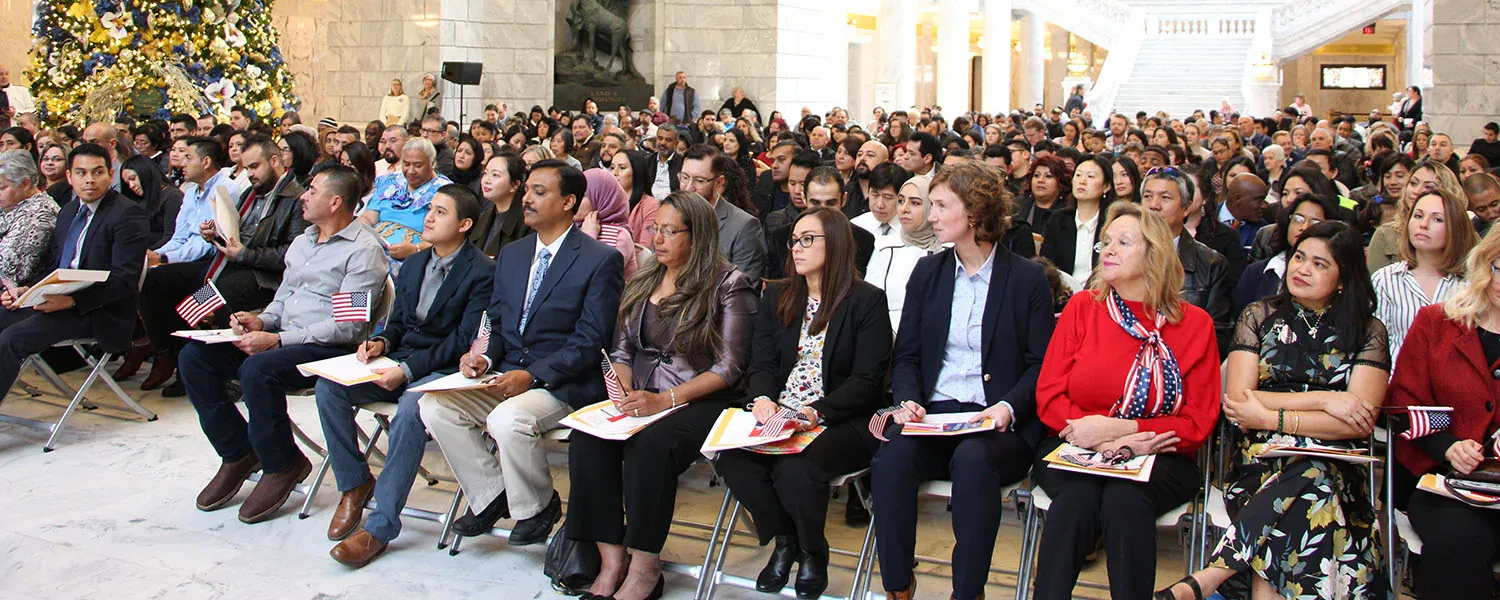 An upside-down person walks on their hands down cement steps while a diverse collection of people sitting on the steps look on and take photos.