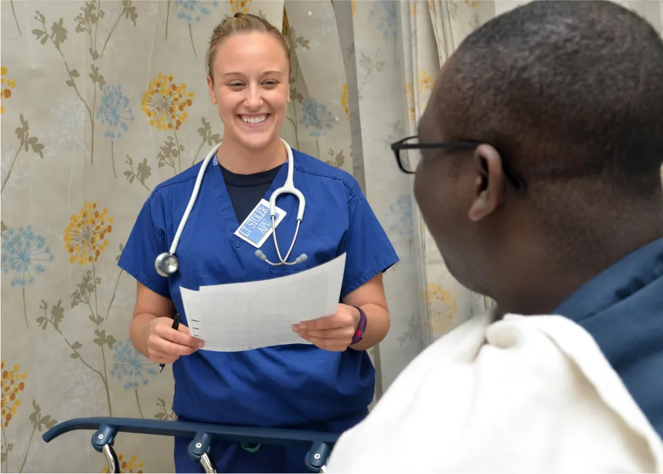 Photo of healthcare worker speaking with patient in a bed.