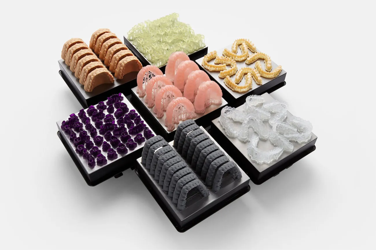 A series of seven adjacent trays contains different types of dental fixtures, including dentures, braces, retainers, and other items. The items are all different colors and shapes.