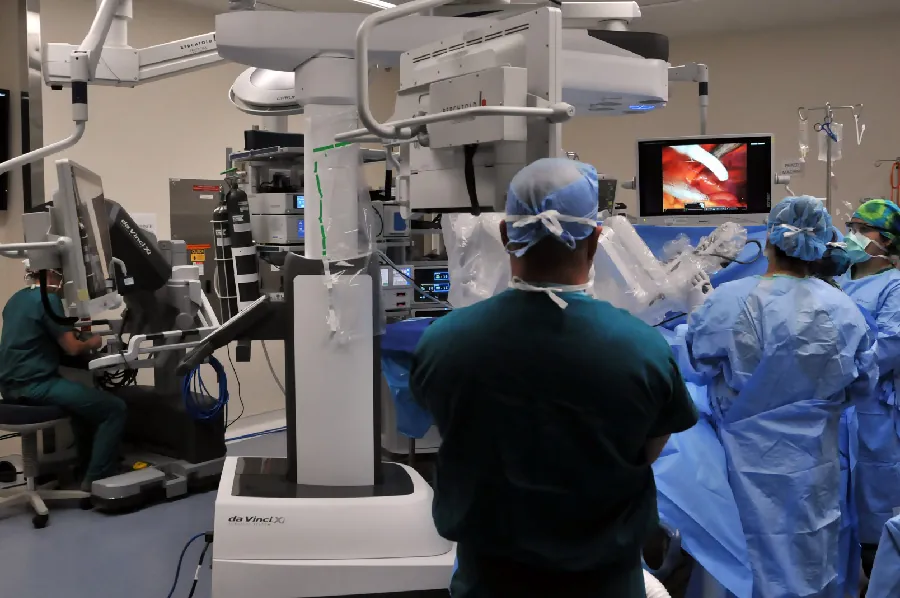 Image of medical personnel watching a robotic arm perform surgery.
