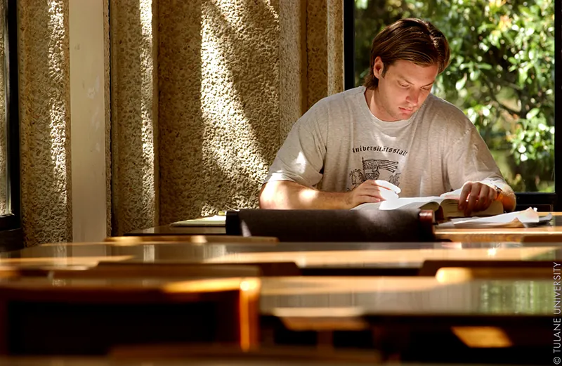 Student writer Shawn Krukowski reads a book at a table outside a classroom building.