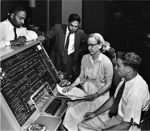 A black and white photo shows Grace Hopper and three others around a large, old computer.