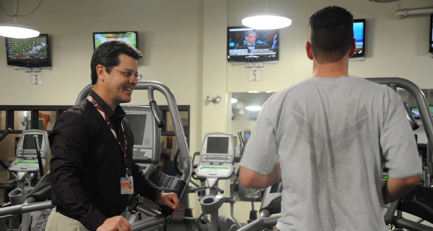 Healthcare professional speaking to patient who is using exercise equipment.