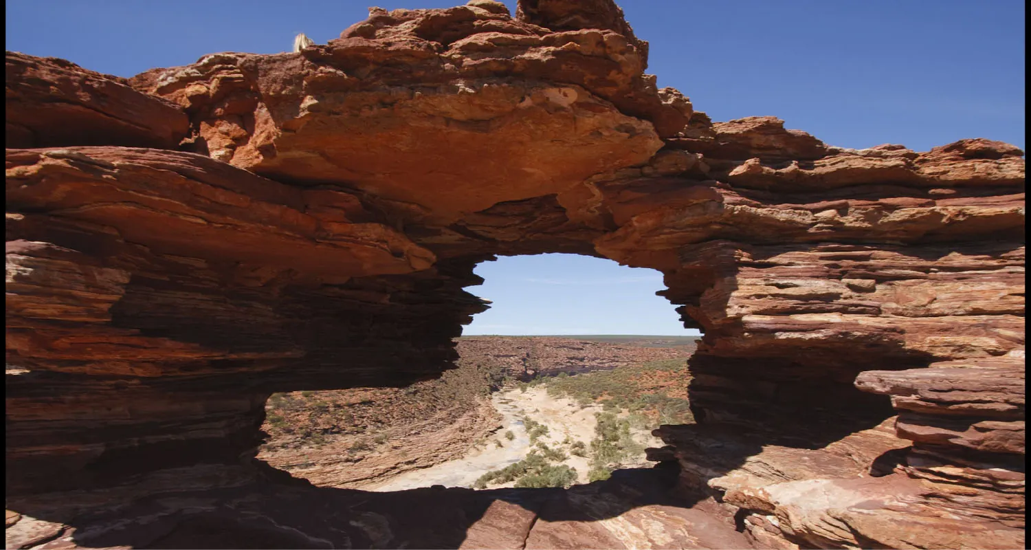 A layered rock formation forming a large circular shape from which a landscape is visible.
