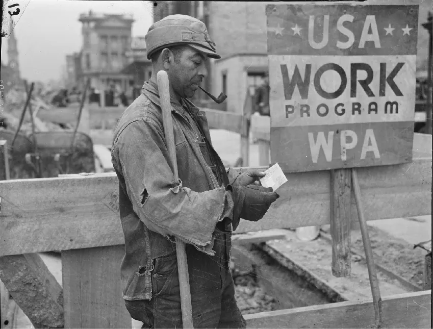 A person wearing work clothes and a hat and smoking a pipe stands outside looking at a piece of paper they hold in their hands. They stand next to a sign that says **USA** work program WPA.
