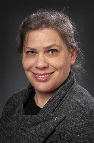 A person in a gray top smiles for a portrait.