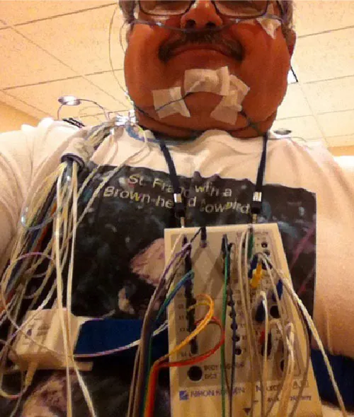 Photo of individual hooked up to a machine with wires taped to various places on his body.
