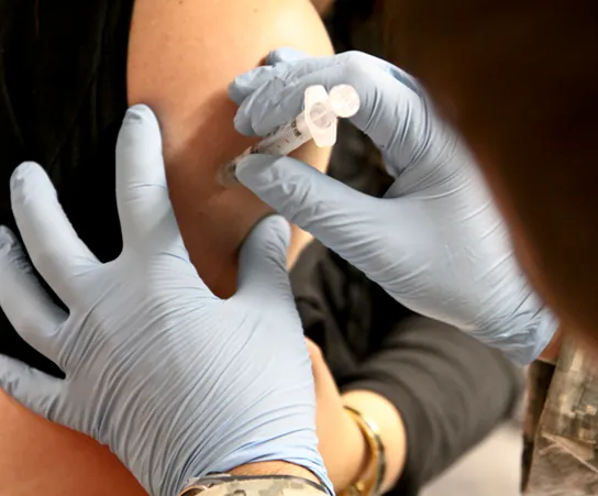 The photo shows a person receiving an injection in the arm.