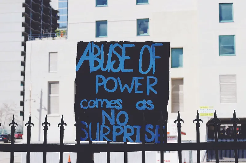 This image shows a hand-painted sign that says “Abuse of power comes as no surprise.”