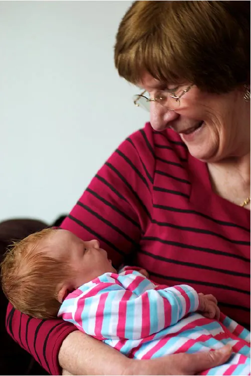 Infant being held and looking up at adult smiling at them.