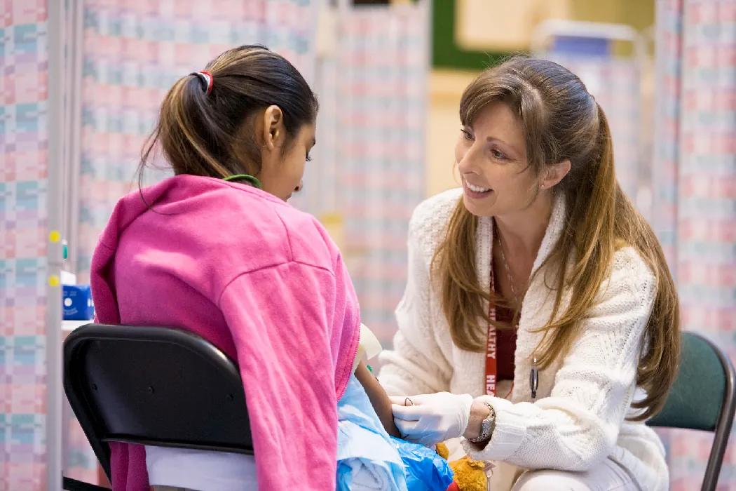 A nurse and a client sit across from one another in folding chairs. The nurse smiles and looks the client in the eye.