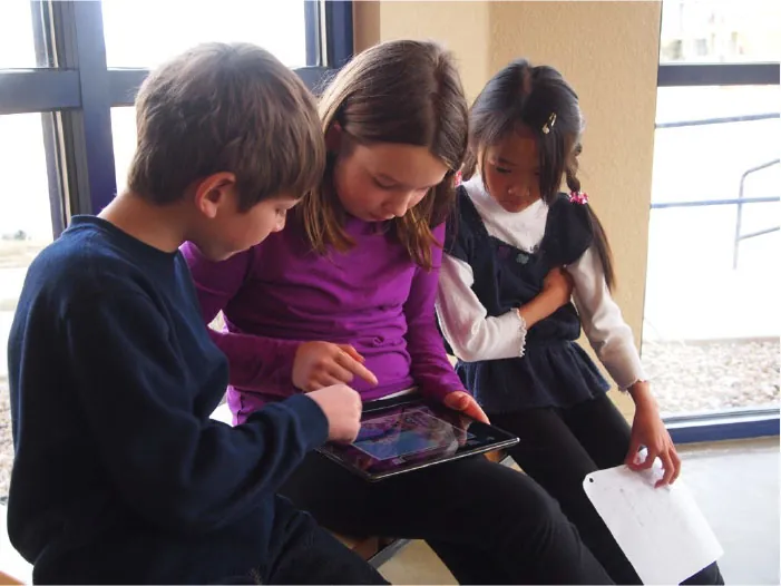 Photo of three young children looking down at an iPad.