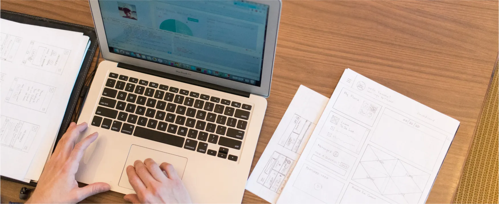 An open laptop with a person's hands on the trackpad are shown.