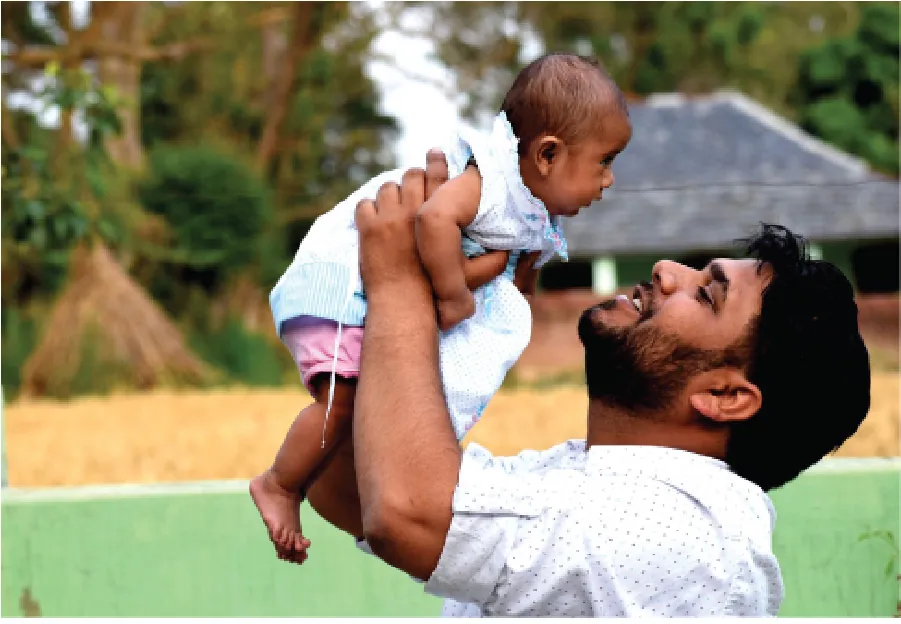 Photo of individual holding an infant up in the air, smiling at them.