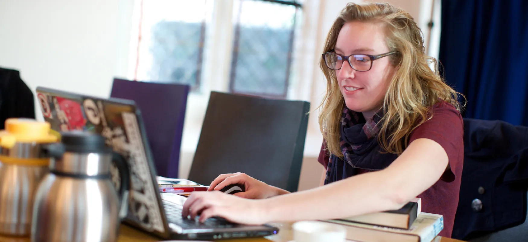 A student works on their laptop computer, while their left elbow rests on two books.