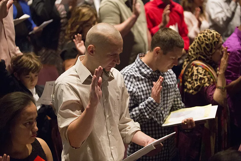 A group of people stand in rows, raising their right hands and holding papers in their left hands.