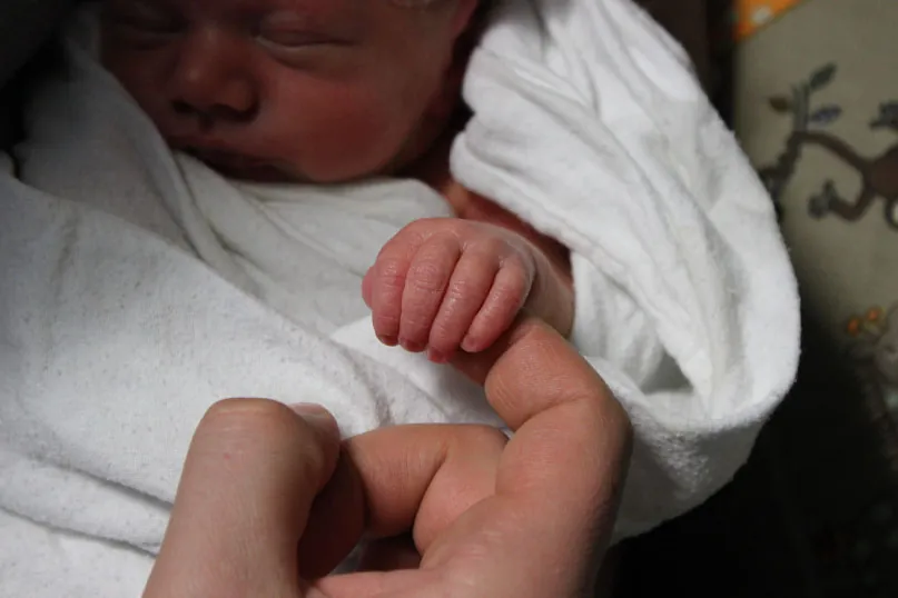 Photo of infant grasping person’s finger.