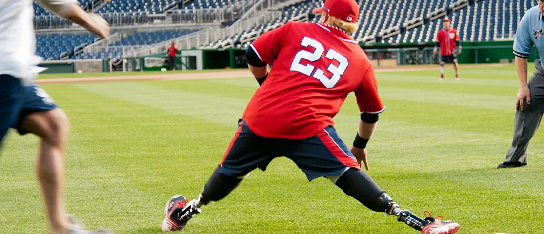 Photo shows a man with prosthetic legs stretching out while playing baseball.