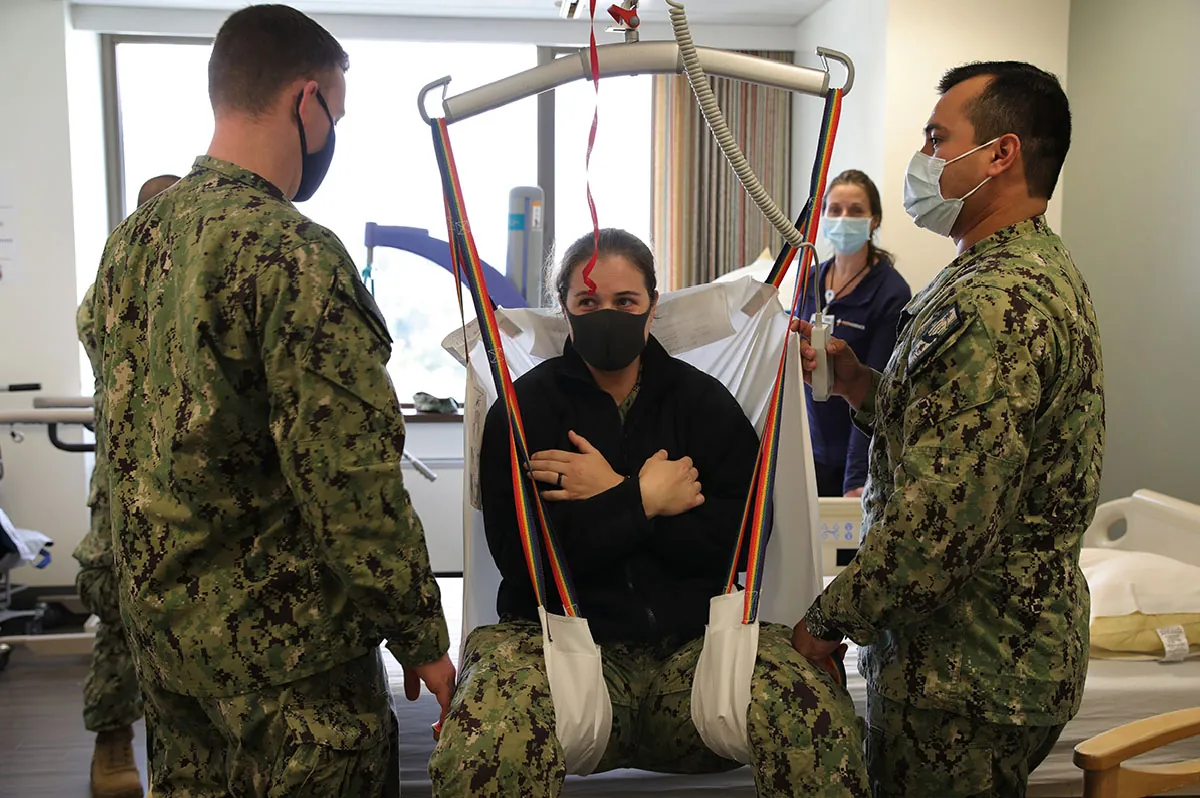 Military members use a sling lift on a colleague.